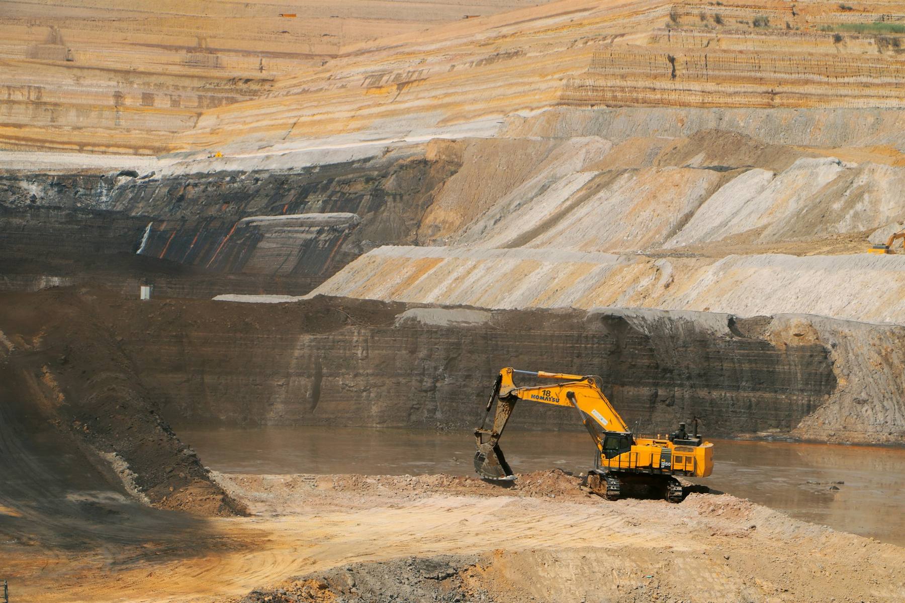 Yellow excavator working a bench in a large open-pit mine